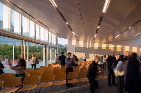 The Meeting Room's double height glazing and a perforated wood ceiling open to the garden. Exterior granite pavers extend into the Meeting Room interior through large sliding glass doors, allowing people to move freely between indoor and outdoor spaces.