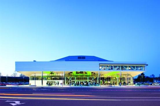The second-floor cladding is composed of white 22 gauge metal panels. Staggering the panels, some of which are slightly recessed, adds texture to the surface. The swell of the roof?supported inside by massive steel trusses?is clad in a similar material with smaller-scale horizontal metal ribs.