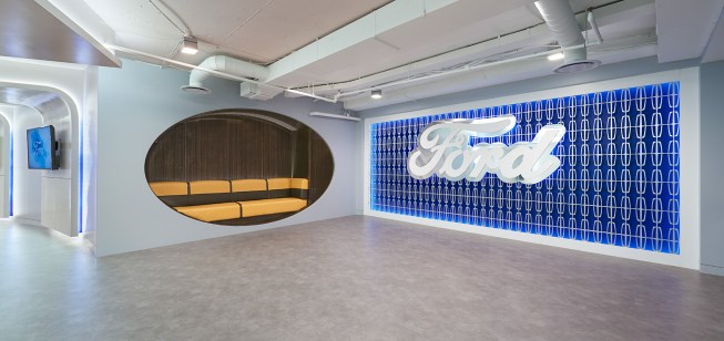 The reception area’s alcove bench seating conveys rich, nostalgic memories of Ford’s 1950’s cars, known for luxury and comfort, and assimilates an actual Ford seat, complete with stiching. The throwback, continuous-curved banquette features Keding Enterprises veneer paneling and Designtex’s upholstery wrapped cushion seating.