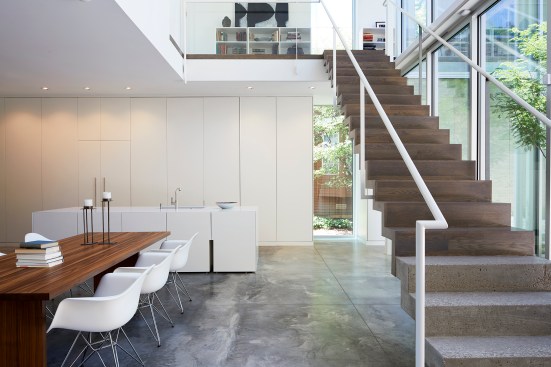 An open stair in the kitchen area—concrete at the base, transitioning to wood partway up—leads to the upstairs bedrooms.
