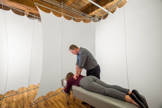 Chiropractor works on woman inside stretched white fabric treatment room