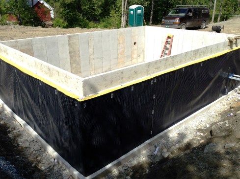 Figure 3. The 12-inch-thick foundation wall was poured with an 8-inch-wide shelf to support the stone veneer. Stego Wrap was run up the foundation’s exterior face and then folded onto the stone shelf. To protect the Stego from puncturing during backfilling, a dimpled drainage mat was installed against the wall. Later, 12-inch-thick EPS foam would be installed on the foundation’s interior, which would create a continuous insulation plane from the foundation up to the framed wall.