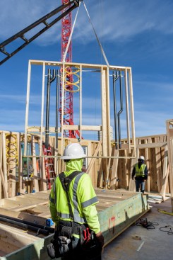 A crane drops a wall panel with shop-installed plumbing and electrical wiring into place at Katerra's K90 project.
