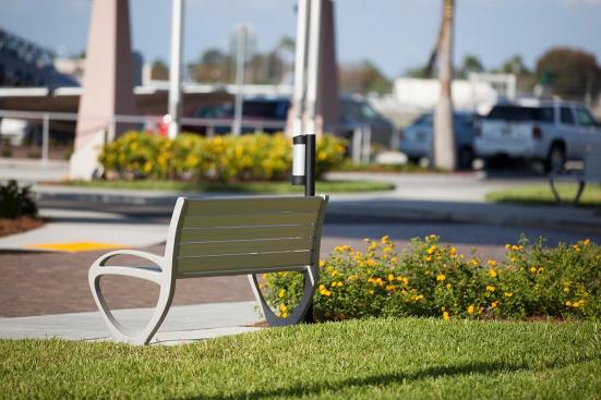 Trio Bench shown in 6 foot, backed configuration with Aluminum Texture powdercoated frame and clear anodized aluminum slats; Buttler Ash Receptacle shown in medium, pole-mount configuration with Black Texture powdercoated endcaps and Silver Anodized powdercoated cylinder at Page Field, Fort Meyers, Florida