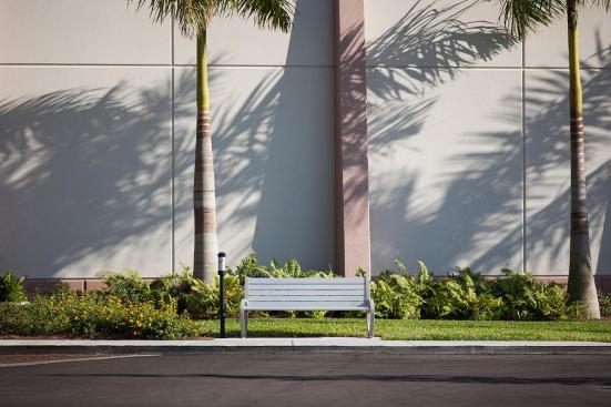 Trio Bench shown in 6 foot, backed configuration with Aluminum Texture powdercoated frame and clear anodized aluminum slats; Buttler Ash Receptacle shown in medium, pole-mount configuration with Black Texture powdercoated endcaps and Silver Anodized powdercoated cylinder at Page Field, Fort Meyers, Florida