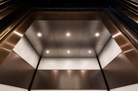 Elevator ceiling shown in Stainless Steel with Sandstone finish; LED downlights shown in LEVELe-104 Elevator Interior with main panels in ViviChrome Chromis, White interlayer, Opalex finish; accent panels in Fused Nickel Silver, Sandstone finish at 1000 Broadway, Portland, Oregon