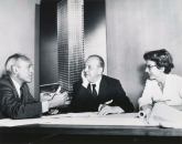 Philip Johnson, Ludwig Mies van Der Rohe, and Phyllis Lambert discuss the Seagram in front of an image of the building model soon after she helped the architects win the commission in 1955.